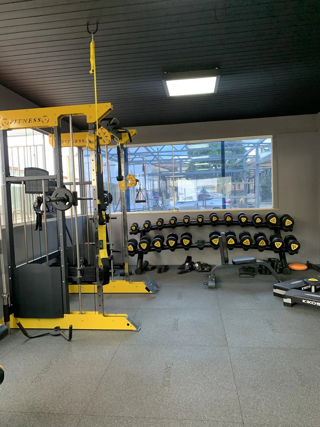 Salão de musculação com rack de halteres amarelos e estação de cabos
